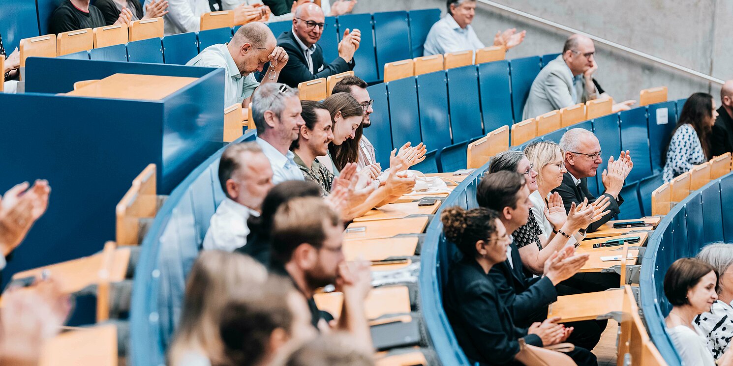 Blick in einen Hörsaal mit klatschenden Zuhörer.