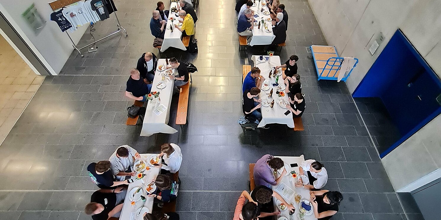 Blick von oben in ein Foyer, in dem Personen an Tischen sitzen.