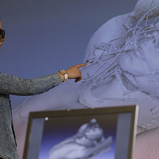 Zwei Frauen schauen mit VR-Brillen auf eine animierte Statue, die an eine Wand projiziert ist. 